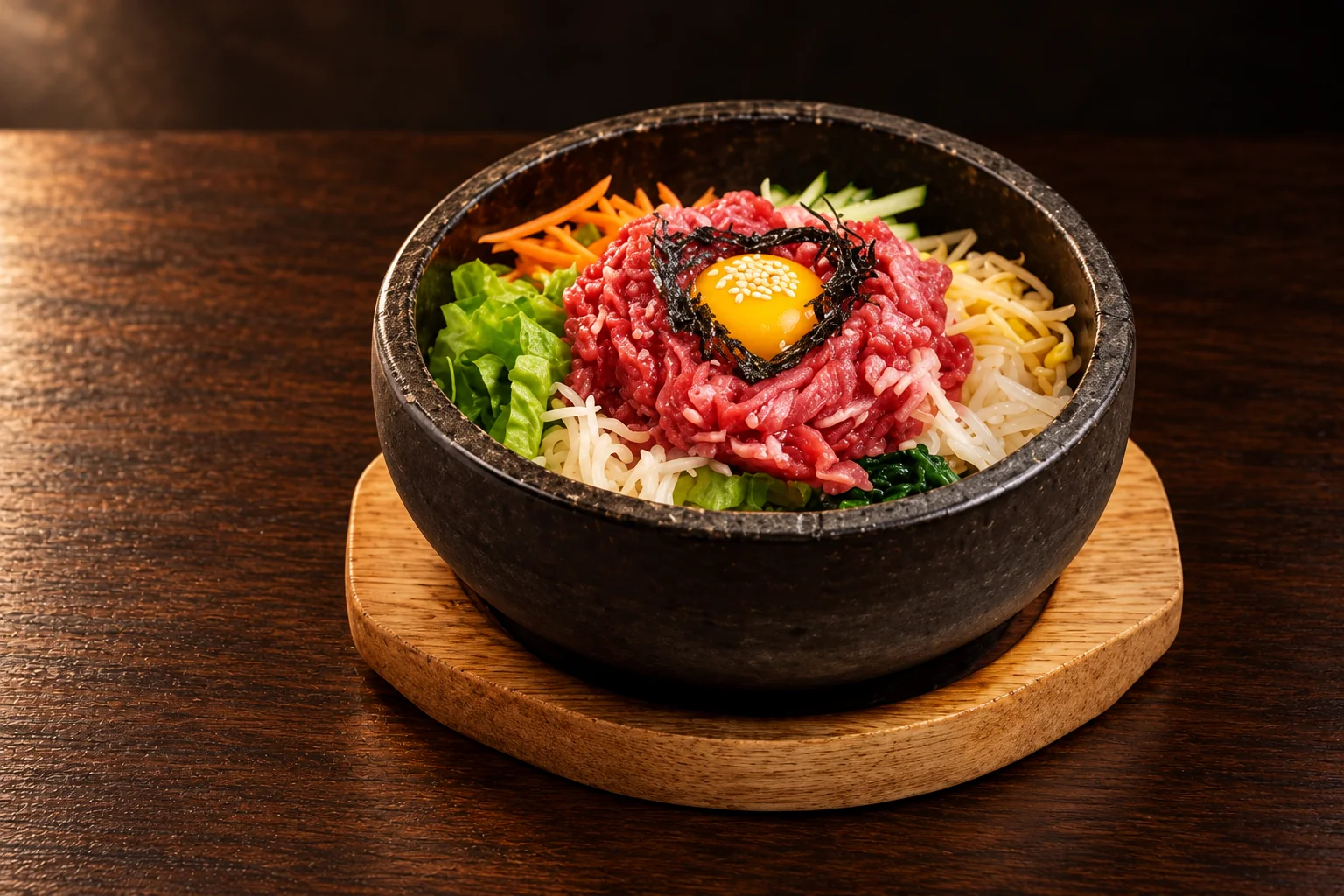 Beef tartare bibimbap in a black stone bowl on a wooden stand